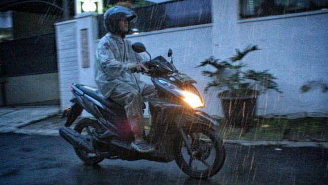 Pengendara motor melaju di tengah hujan deras.