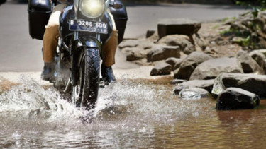Pengendara motor melintasi genangan air.
