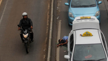 Pengendara motor melintas di dekat sopir taksi yang tertidur saat melakukan demo menolak keberadaan angkutan umum online di di Jalan Gatot Subroto, Senayan, Jakarta, Selasa(22/3/2016).