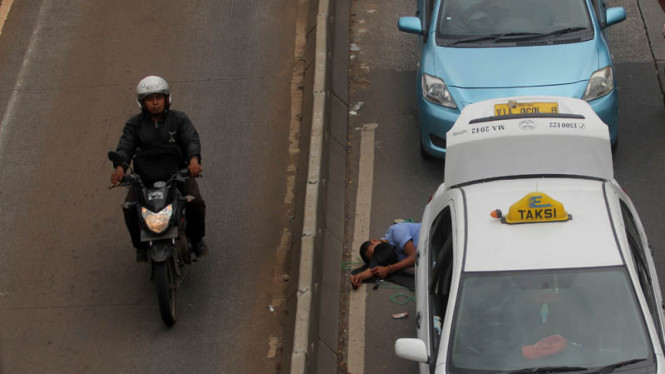Pengendara motor melintas di dekat sopir taksi yang tertidur saat melakukan demo menolak keberadaan angkutan umum online di di Jalan Gatot Subroto, Senayan, Jakarta, Selasa(22/3/2016).