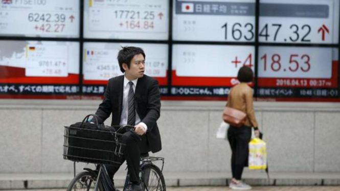 Pengendara sepeda di depan papan Bursa Saham Tokyo.