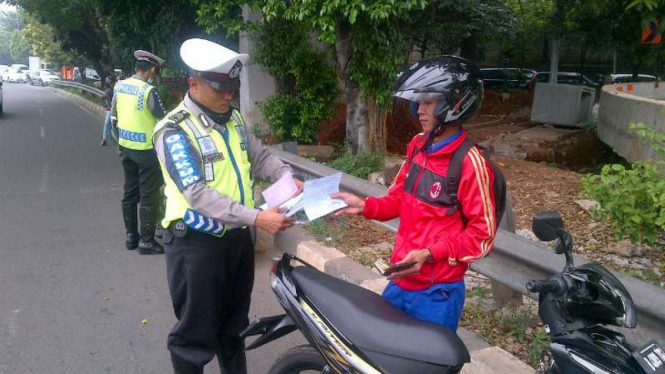 Petugas memberi sanksi tilang ke pengendara motor.