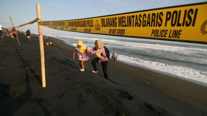 Sejumlah wisatawan berjalan di belakang garis polisi yang dipasang di bibir Pantai Trisik, Kabupaten Kulon Progo, Yogyakarta, Minggu (10/7/2016). 