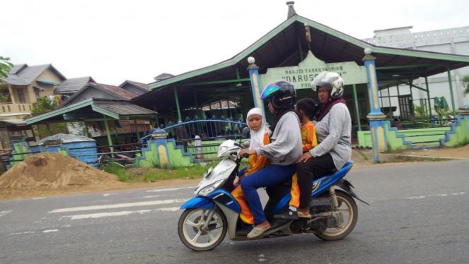 Keluarga berboncengan sepeda motor.