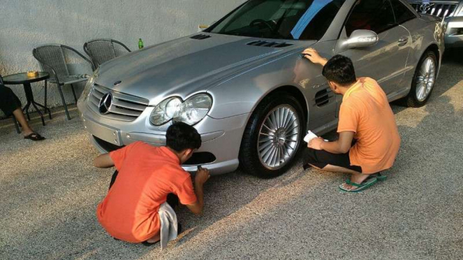 Dua orang sedang mengecat mobil.
