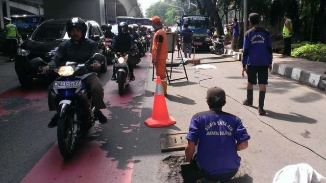Pasukan oranye dan biru membersihkan gorong-gorong di kawasan Kuningan, Jakarta.