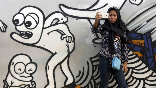 Seorang gadis sedang selfie dengan latar lukisan mural di Jakarta