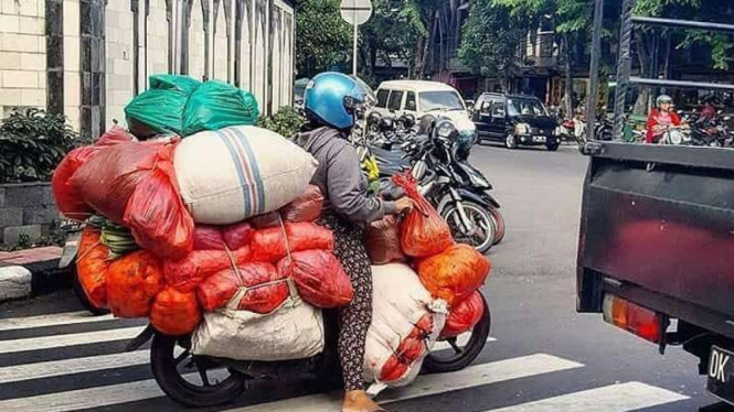 Emak-emak bawa banyak barang naik motor.