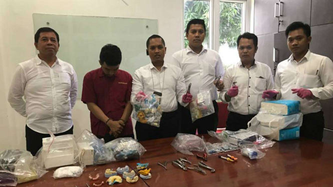 Rudi (baju merah) saat di ciduk polisi di lokasi praktiknya.