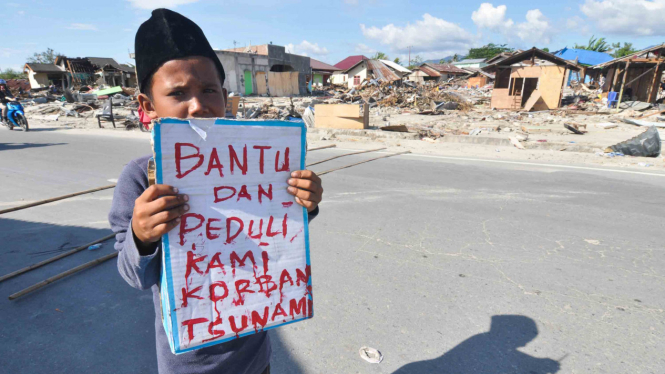 Seorang anak korban gempa dan tsunami berdiri  mengharapkan sumbangan dari pengendara yang lewat di Palu, Sulawesi Tengah