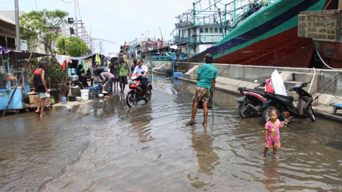 Warga melintasi genangan air banjir rob di kawasan akses pintu masuk menuju pelabuhan Muara Angke, Jakarta Utara