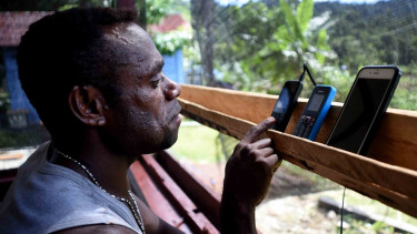 Seorang warga menggunakan telepon genggamnya di pelosok Mosairo, Nabire, Papua