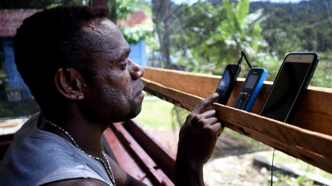 Seorang warga menggunakan telepon genggamnya di pelosok Mosairo, Nabire, Papua