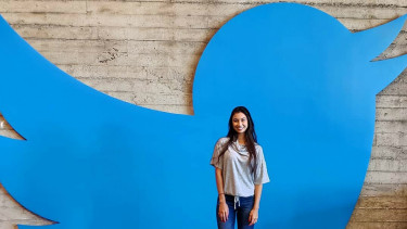 Seorang pengunjung berpose di depan logo Twitter.