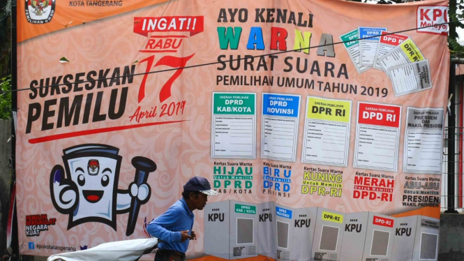Seorang pria melintasi baliho sosialisasi Pemilu 2019.