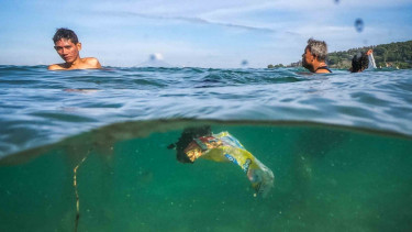 Sejumlah pengunjung berenang di dekat sampah plastik.
