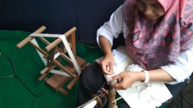 Wanita sedang mengurai serat-serat dari kepompong putih