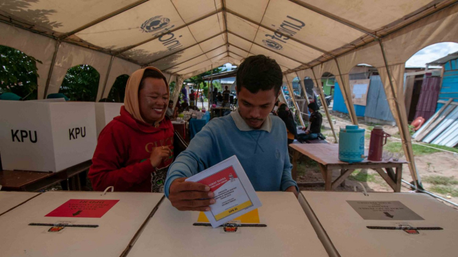 Seorang warga korban bencana memasukkan surat suara ke kotak suara usai menyalurkan hak suaranya di tenda pengusian saat pemungutan suara Pemilu 2019, di TPS 01 Kelurahan Petobo , Palu, Sulawesi Tengah