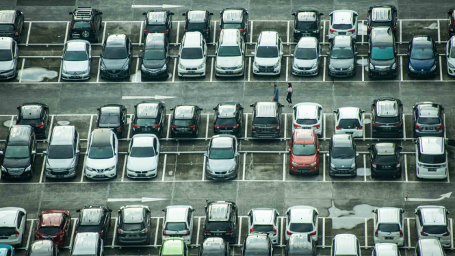 Warga berjalan di antara mobil yang terparkir di Jakarta.