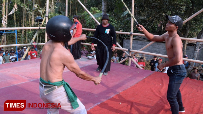 Dua orang saling mencambuk bergantian di Tradisi Tiban yang dilaksanakan Desa Sawentar Kecamatan Kanigoro Kabupaten Blitar, Selasa (24/9/2019). (Foto: Sholeh/TIMES Indonesia)