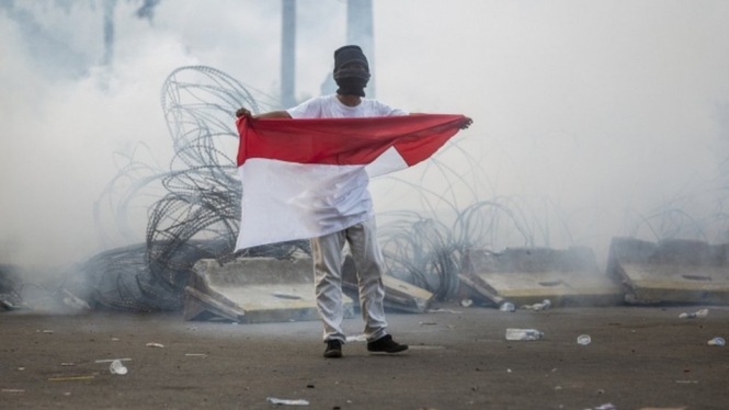Seorang pelajar membentangkan bendera merah-putih dalam demonstrasi di dekat gedung DPR/MPR, Jakarta, pada Senin (30/09). - Getty Images
