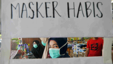 Petugas apotek memasang pengumuman stok masker habis.