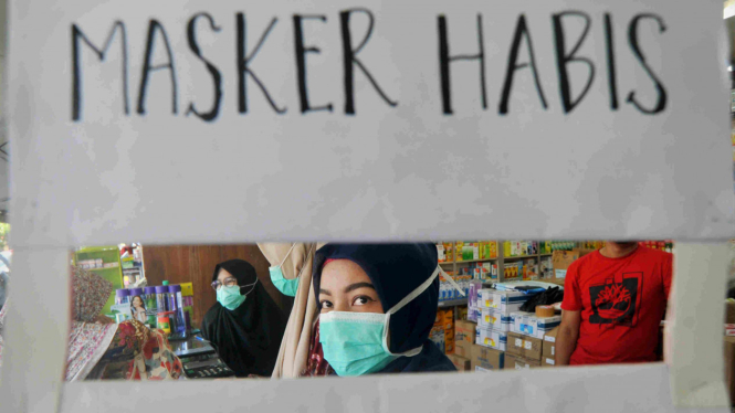 Petugas apotek memasang pengumuman stok masker habis.