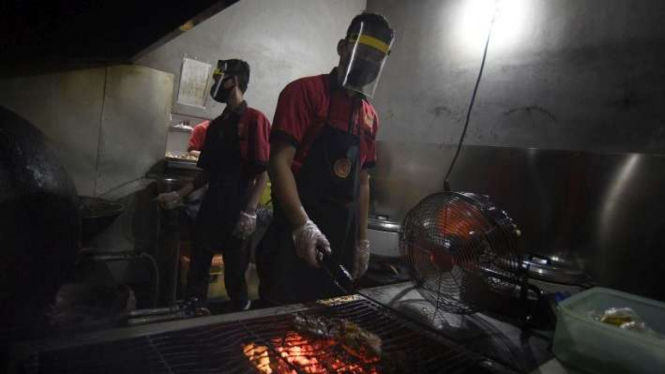 Karyawan mengenakan face shield saat mempersiapkan pesanan makanan di restoran