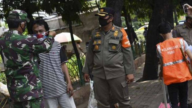 Petugas gabungan memasangkan masker kepada seorang warga (Foto ilustrasi)