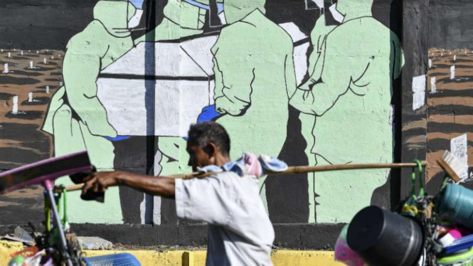 Pedagang yang tak pakai masker melintas di depan mural waspada Corona, di Tebet