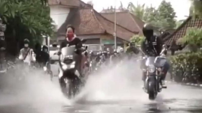 Emak-emak naik motor melintasi genangan air.