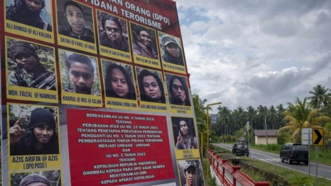 Sejumlah pengendara mobil melintas di depan baliho yang menampilkan buronan anggota Mujahidin Indonesia Timur (MIT) Poso di Desa Tambarana, Poso Pesisir Utara, Kabupaten Poso, Sulawesi Tengah, Rabu, 23 Desember 2020.
