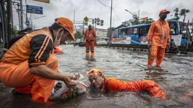 Petugas PPSU membersihkan sampah yang menyumbat saluran air.