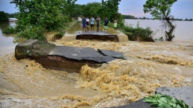 Warga berdiri di atas sebuah jalan yang rusak oleh banjir setelah hujan lebat di kecamatan Nagaon, negara bagian Assam, India.