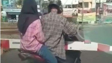 Sepeda motor sepasang kekasih ini terjepit palang pintu kereta api