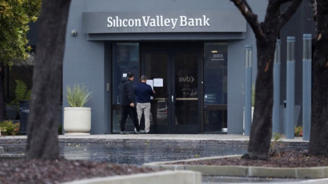 Seorang pria memasang tanda di pintu Silicon Valley Bank saat seorang penonton mengawasi di kantor pusat bank di Santa Clara, California, AS, 10 Maret 2023.